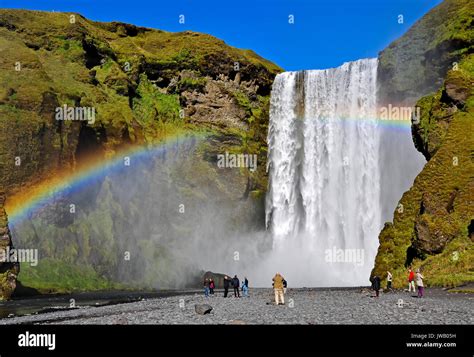 Skogafoss waterfall and rainbow with incidental tourists. Skogafoss is ...