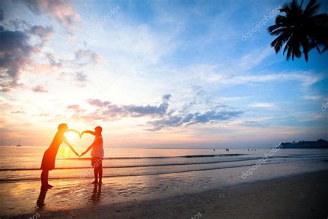 Young couple holding hands heart-shaped on the sea beach at sunset. — Stock Photo © dimaberkut ...