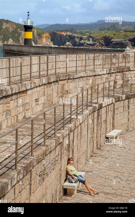 Woman enjoying the sunshine, sitting by the harbour walls in Comillas ...