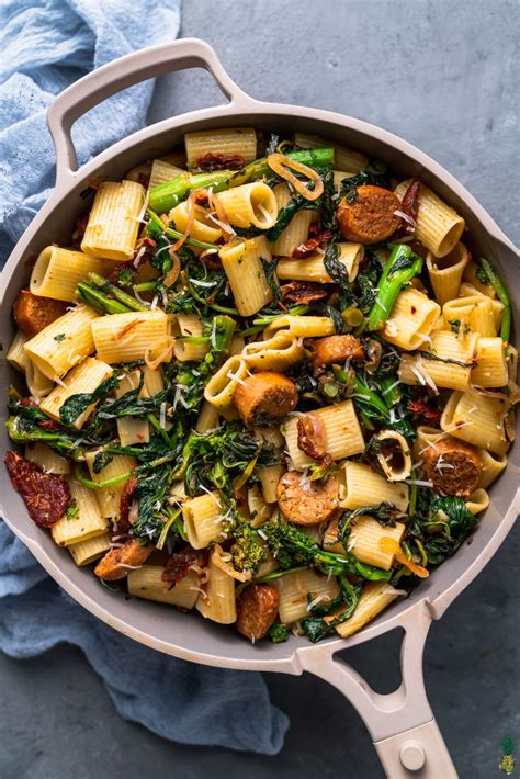 a skillet filled with pasta, spinach and sausage