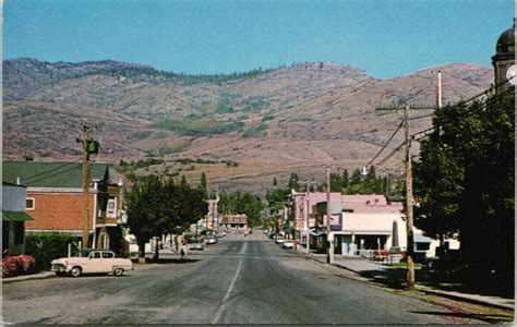 an old photo of a town with mountains in the backgrouds and cars parked on the street