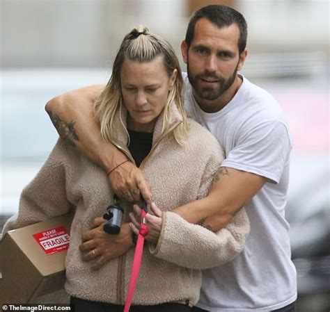 Robin Wright, 53, keeps her head down as her husband Clement Giraudet, 34, holds on to her ...