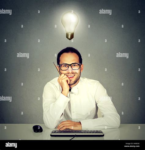 Smiling young handsome man sitting in front of computer keyboard with light bulb over his head ...