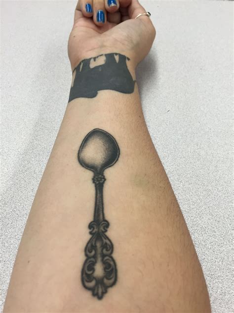 a woman's arm with a black and white tattoo on it, holding a spoon