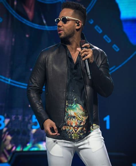 a man in black jacket and sunglasses holding a microphone on stage with other people behind him