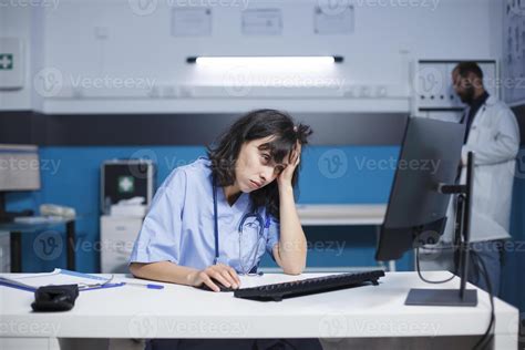 Caucasian woman in blue scrubs, tiredly studying medical data on her ...