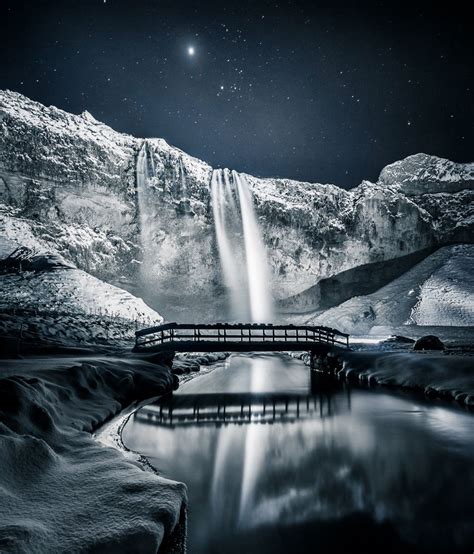 snowy, wintry scene at southern Iceland’s Seljalandsfoss waterfall, which is illuminated by ...