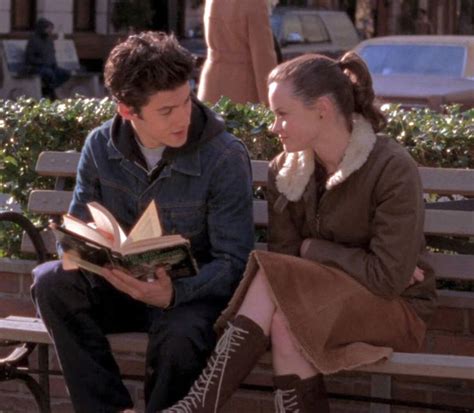 a young man and woman sitting on a bench reading a book in front of them