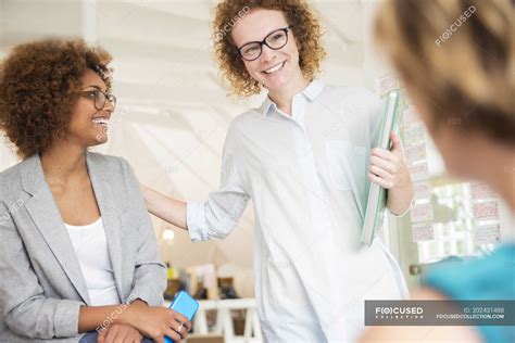 Women smiling and talking in office, holding smart phone and laptop — Coworker, Creative ...