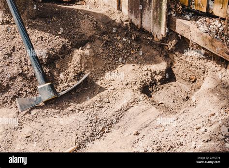 mattock gardening tool to dig the ground and chop weeds left next to fence and hole in the ...