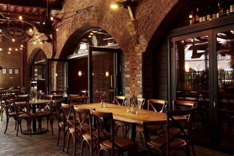 an indoor dining area with tables, chairs and lights hanging from the brick ceilinging