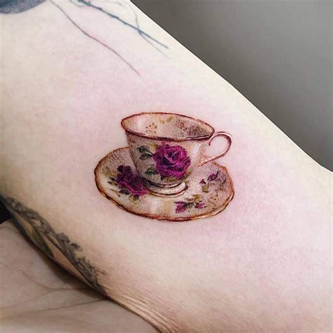 a cup and saucer tattoo on the right side of the left arm, with pink flowers in it