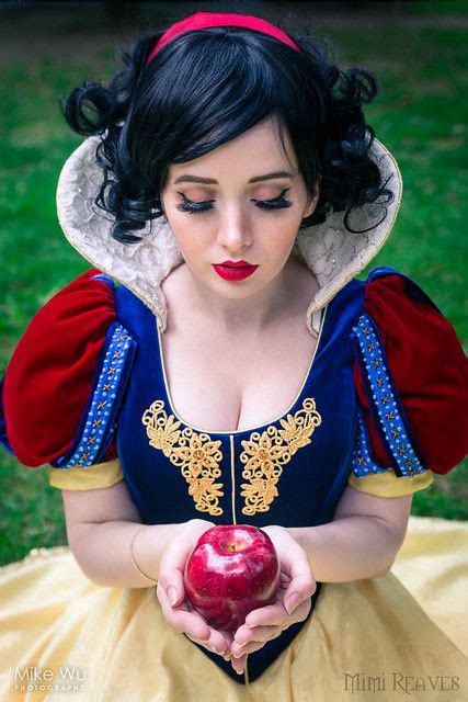 a woman dressed as snow white holding an apple in her hand and looking down at the ground