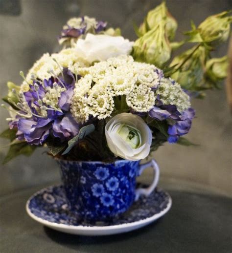 a blue cup filled with white and purple flowers on top of a table next to a plate