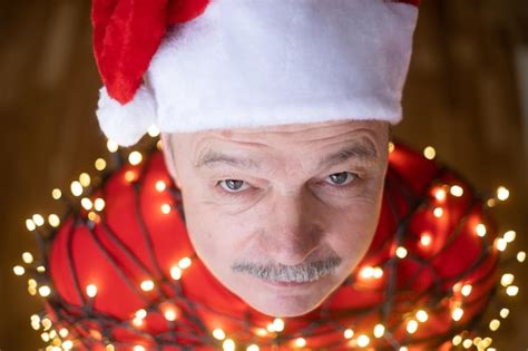 Premium Photo | Senior man in red christmas hat wrapped in garland ...
