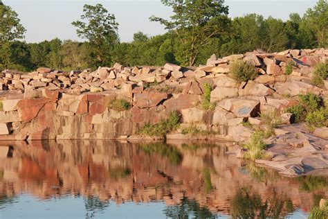 a large rock wall next to a body of water with trees and bushes in the ...