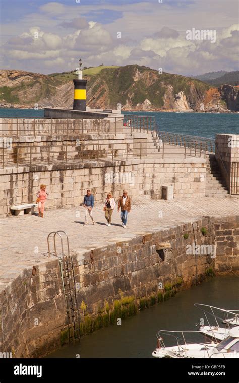 People walking on the harbour in front of the lighthouse at Comillas ...