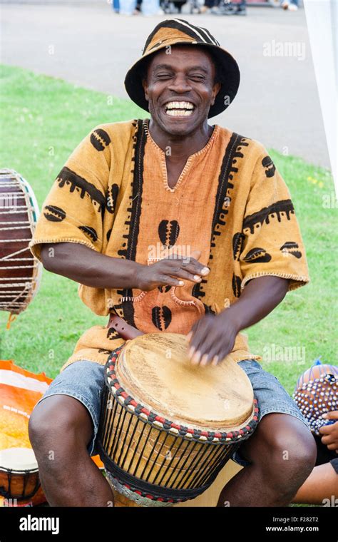 Black African man in shorts, shirt and hat sitting playing bongo drum Stock Photo: 87459010 - Alamy