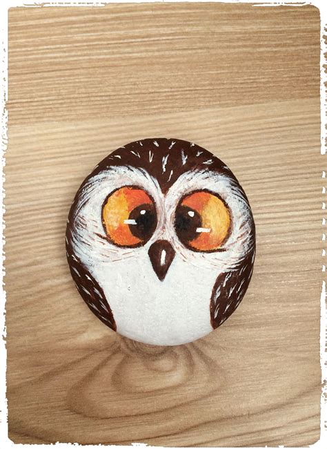 a painted rock with an owl's eyes on it sitting on a wooden surface