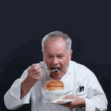 a man eating food from a bowl with a spoon in his mouth while wearing a chef's uniform