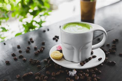 Mug of matcha latte placed on table with scattered coffee beans · Free Stock Photo