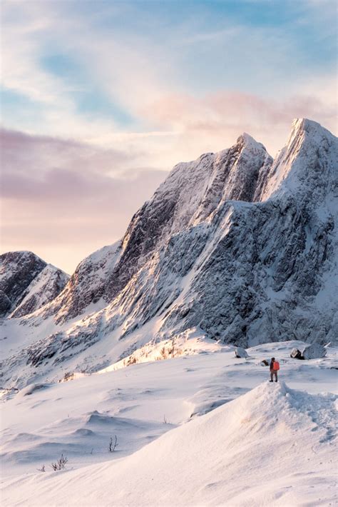 Beautiful winter scenery in Norway. Snow-capped Norwegian mountain with a hiker looking on ...