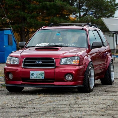 a red subarunt is parked in front of a blue trailer and some trees