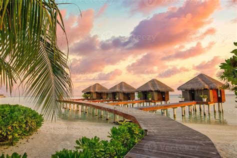 Sunset on Maldives island, luxury water villas resort and wooden pier. Beautiful sky and clouds ...