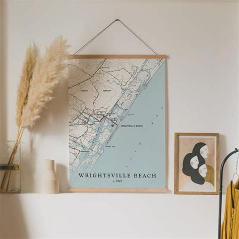 a framed map hangs on the wall next to a vase with dry grass in it