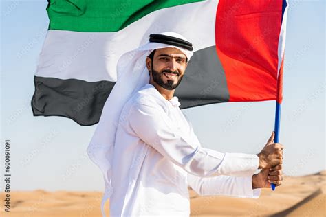 Middle-eastern emirati man wearing arab kandura holding emirati flag in the desert Stock Photo ...