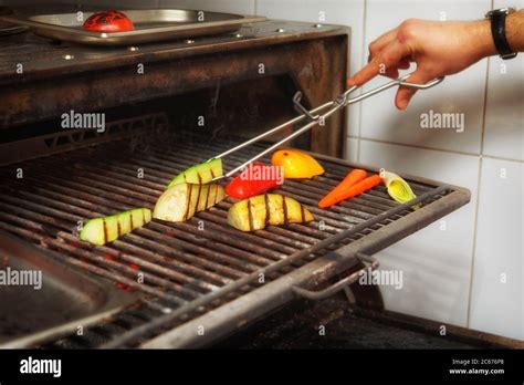 Chef is cooking vegetables in charcoal grill, restaurant kitchen, toned ...