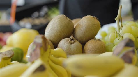 Close-up of kiwi fruits lying on shelf in grocery as unrecognizable man putting one into ...