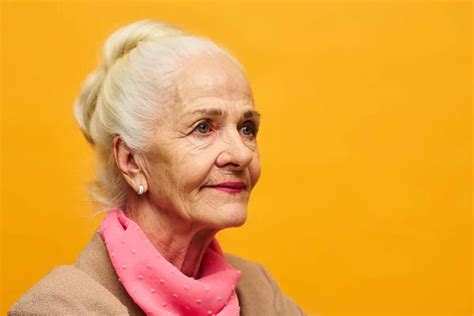 Aged woman with hair bun on head looking forwards while standing in front of camera in isolation ...