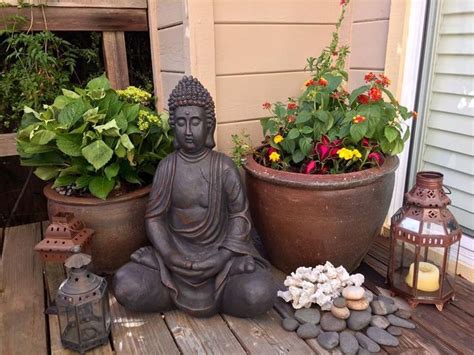 a buddha statue sitting on top of a wooden deck next to potted plants and flowers