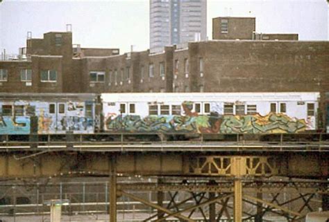 a train with graffiti on it traveling over a bridge in the middle of a city