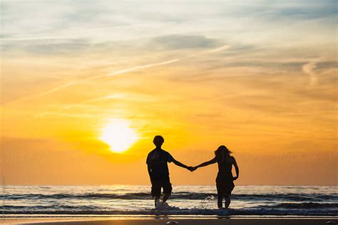 "Silhouettes Of Man And Woman Holding Hands On The Beach At Sunset" by ...