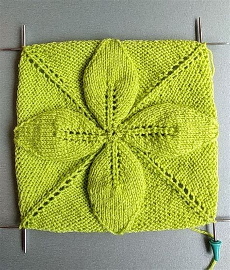 a green knitted object with pins attached to the side and two knitting ...