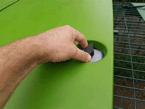 a man's hand is pressing the button on a green table top with a wire fence in the background