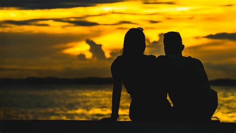 Silhouette of Couple Sitting on Seashore during Sunset · Free Stock Photo