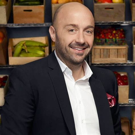 a man in a black suit and white shirt smiles at the camera while standing in front of a shelf ...