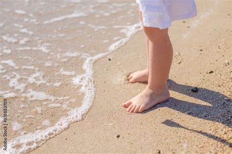 Small baby feet close-up on the sand of the sea beach. Sea water washes ...