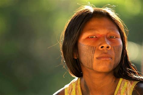 a native american woman with painted on her face and chest looks into the camera while standing ...