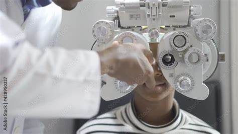 Optician doing optometry eye exam for black african american teen girl patient. Male optometrist ...