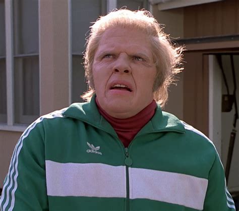 an older man standing in front of a house wearing a green and white ...