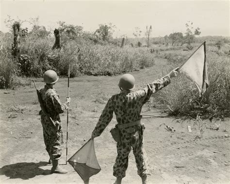 Two soldiers in the foreground use signal flags to communicate with several soldiers hundreds of ...