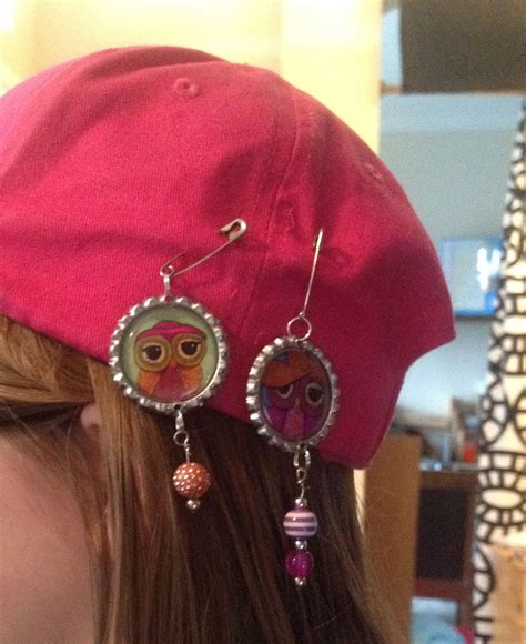 a woman wearing a red hat with owl charms on it's ear and earrings hanging from the side