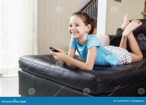 Cute Preteen Girl Watching TV On Couch Using Remote Control. Living Room Interior In Background ...