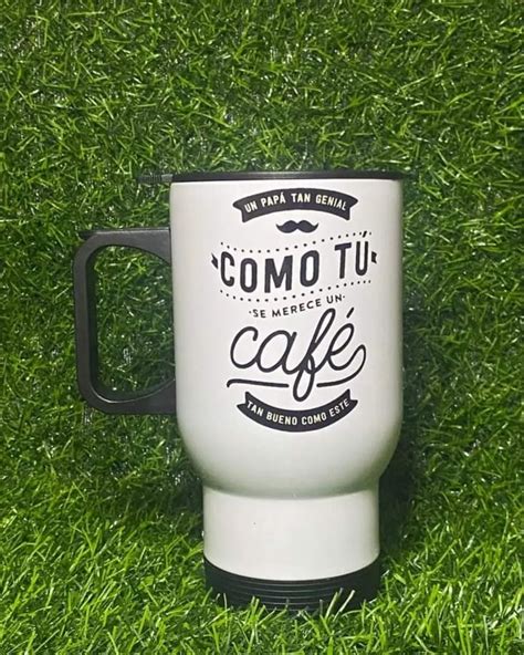 a white coffee mug sitting on top of green grass with the words como tu cafe