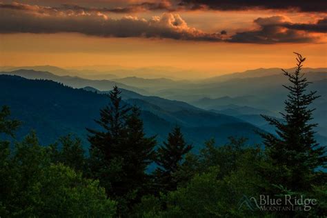 the sun is setting in the mountains with trees on each side and clouds ...