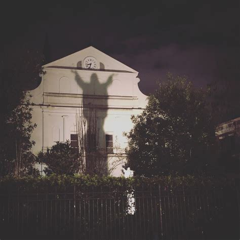 the shadow of a person holding up a clock in front of a building at night